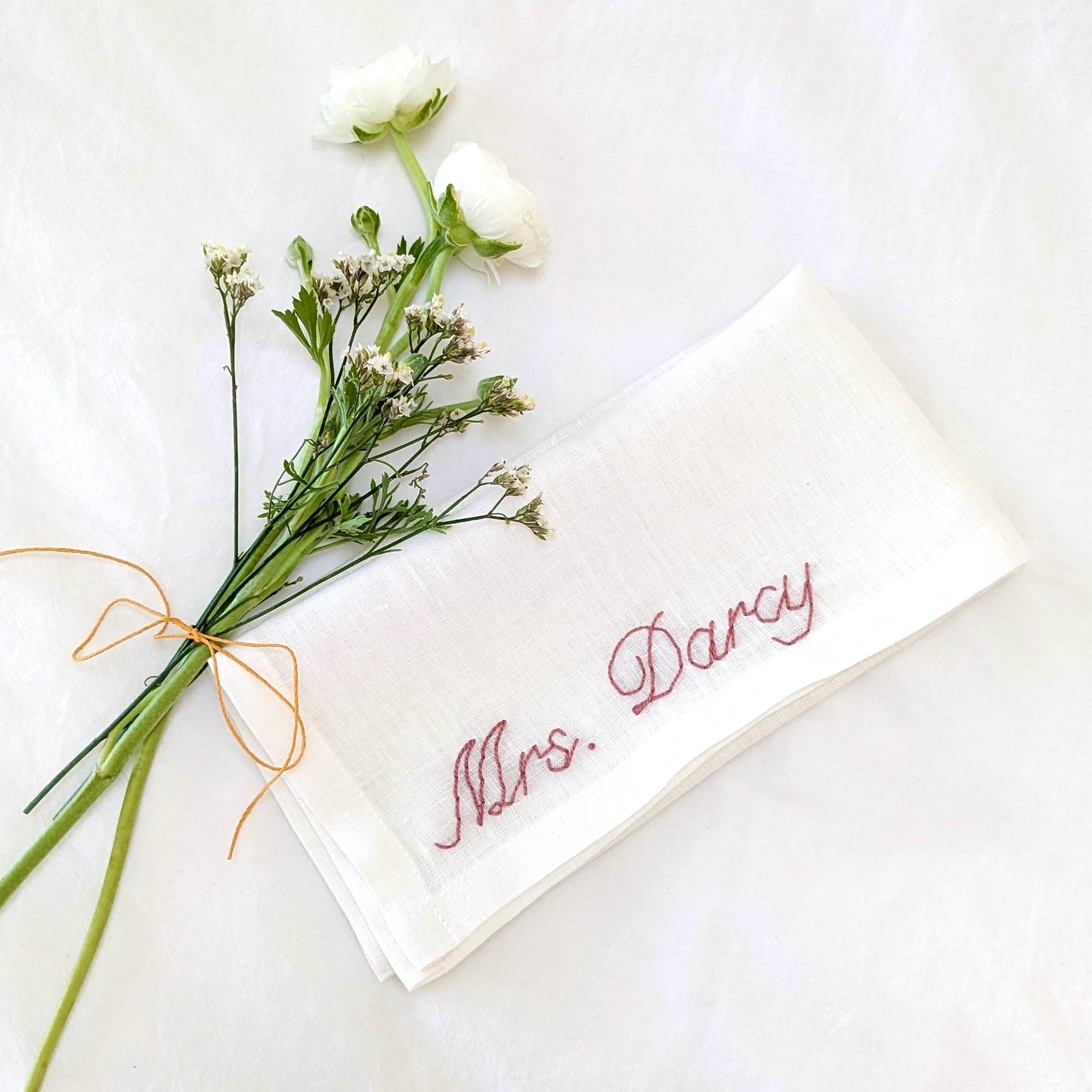 Hand embroidered linen napkin that reads Mrs. Darcy (name is custom)