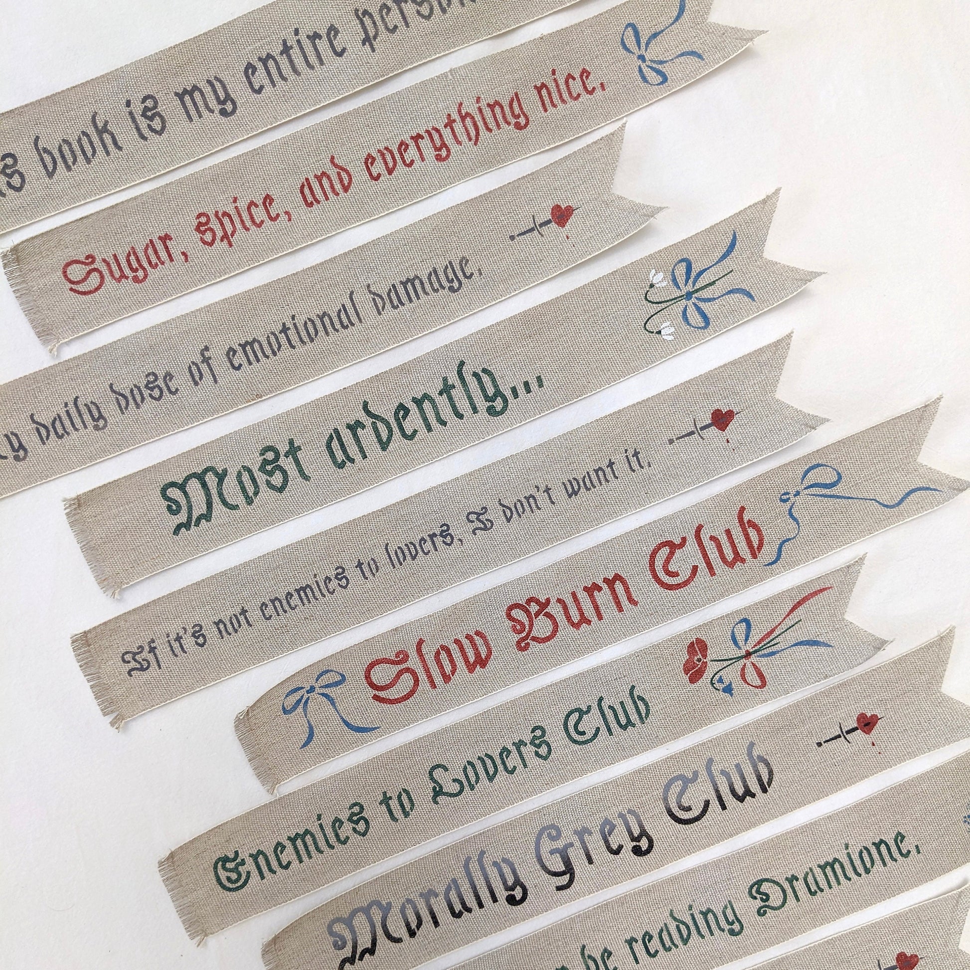 Hand painted linen ribbon bookmarks that read "Sugar, spice, and everything nice" "Slow Burn Club" "Enemies to Lovers Club" and more phrases