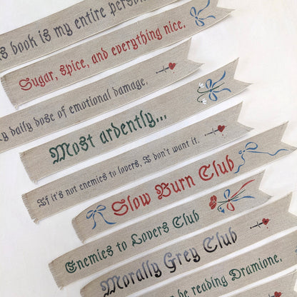 Hand painted linen ribbon bookmarks that read "Sugar, spice, and everything nice" "Slow Burn Club" "Enemies to Lovers Club" and more phrases