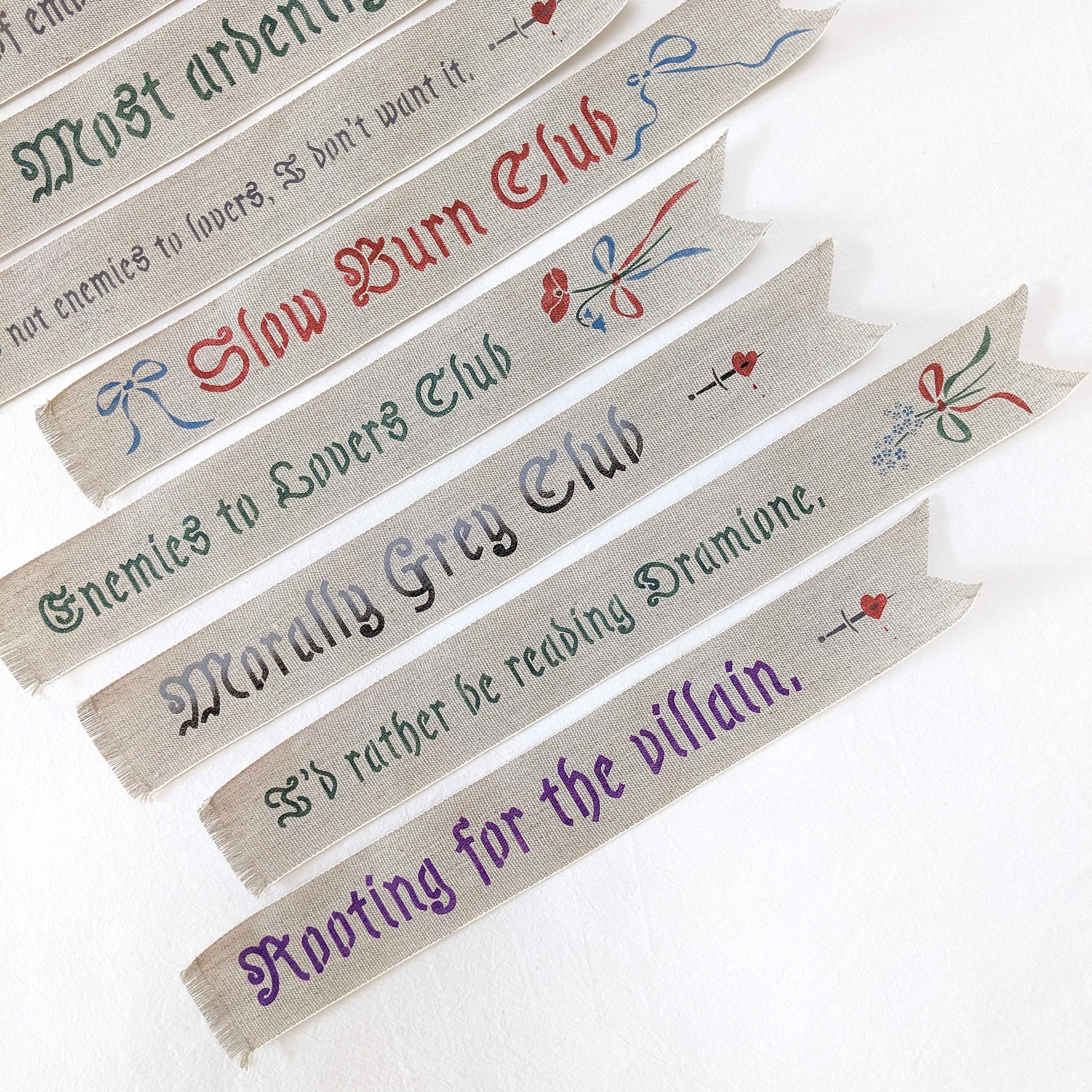 Hand painted linen ribbon bookmarks that read "Sugar, spice, and everything nice" "Slow Burn Club" "Enemies to Lovers Club" and more phrases