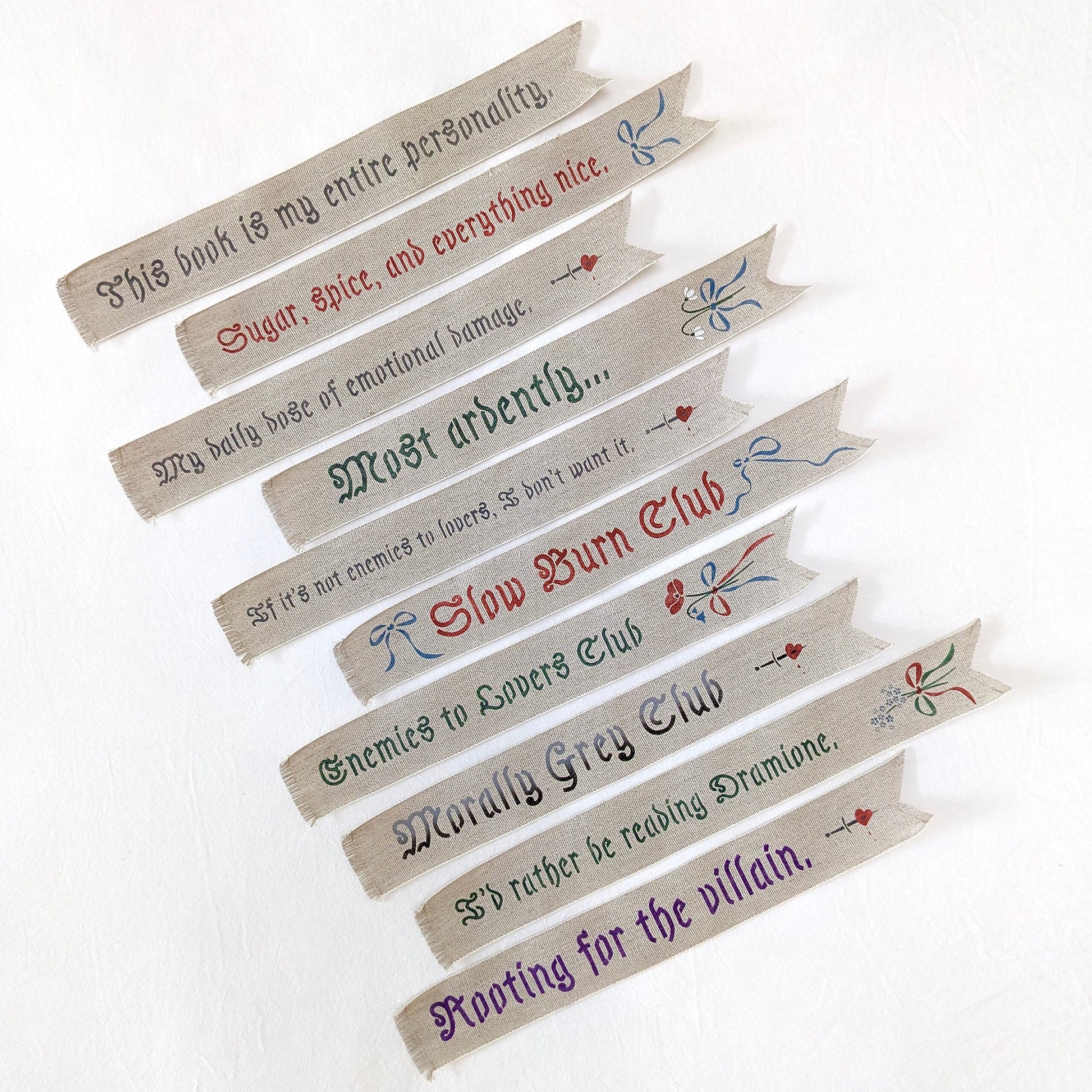 Hand painted linen ribbon bookmarks that read "Sugar, spice, and everything nice" "Slow Burn Club" "Enemies to Lovers Club" and more phrases