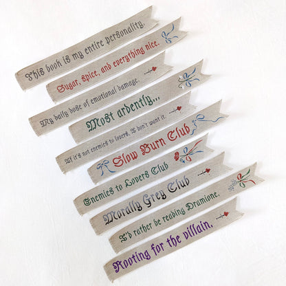 Hand painted linen ribbon bookmarks that read "Sugar, spice, and everything nice" "Slow Burn Club" "Enemies to Lovers Club" and more phrases
