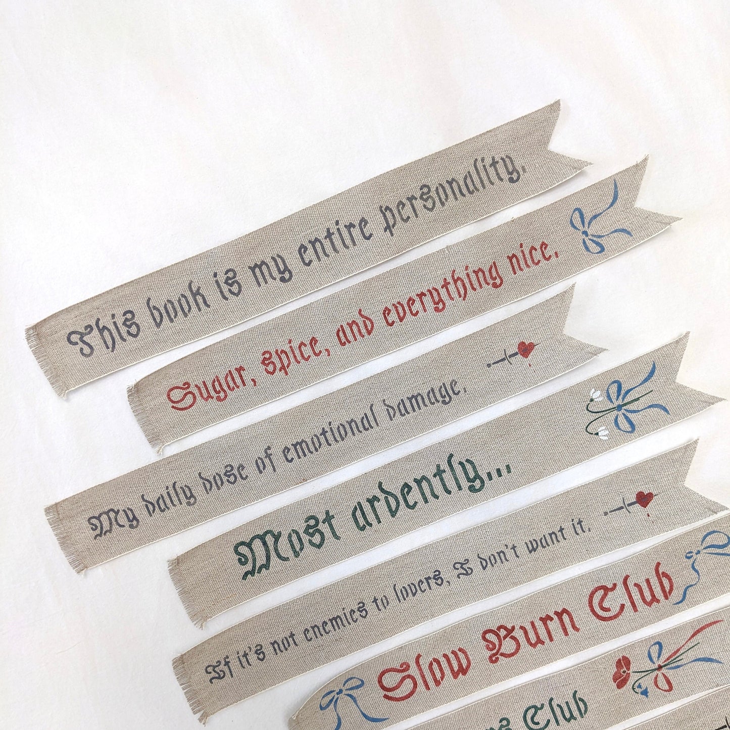 Hand painted linen ribbon bookmarks that read "Sugar, spice, and everything nice" "Slow Burn Club" "Enemies to Lovers Club" and more phrases