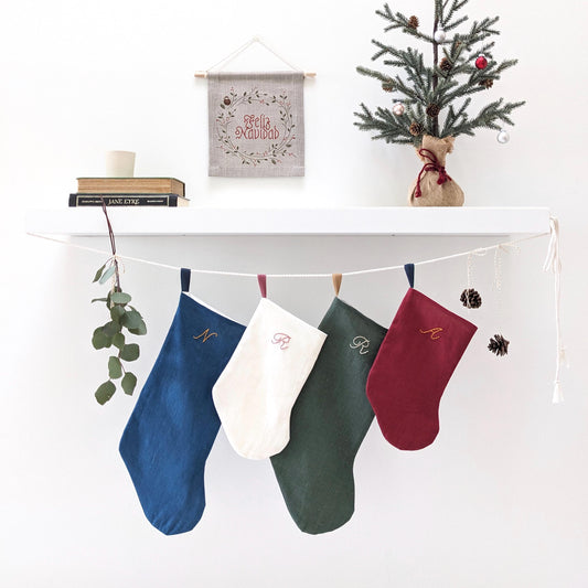 Hand embroidered linen Christmas stocking with personalized initial. Blue with gold embroidery, white with pink, green with white, and red with gold