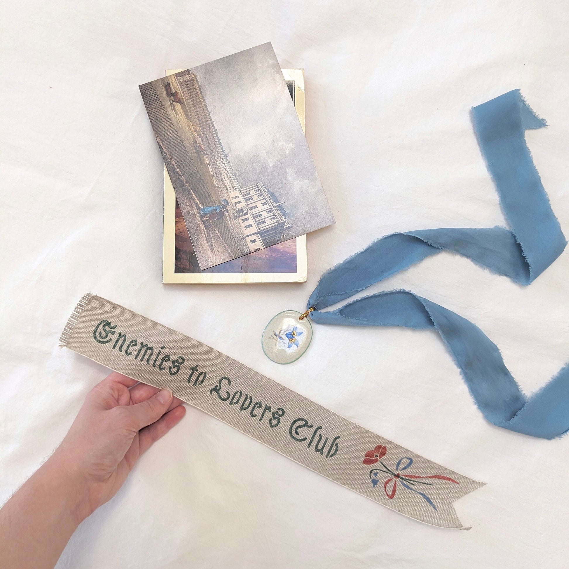Hand painted linen ribbon bookmark that reads "Enemies to Lovers Club"