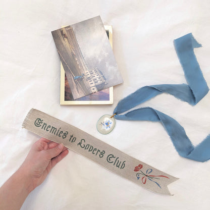 Hand painted linen ribbon bookmark that reads "Enemies to Lovers Club"