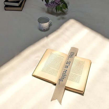 A hand painted linen ribbon bookmark that reads "Shh... I'm reading..."