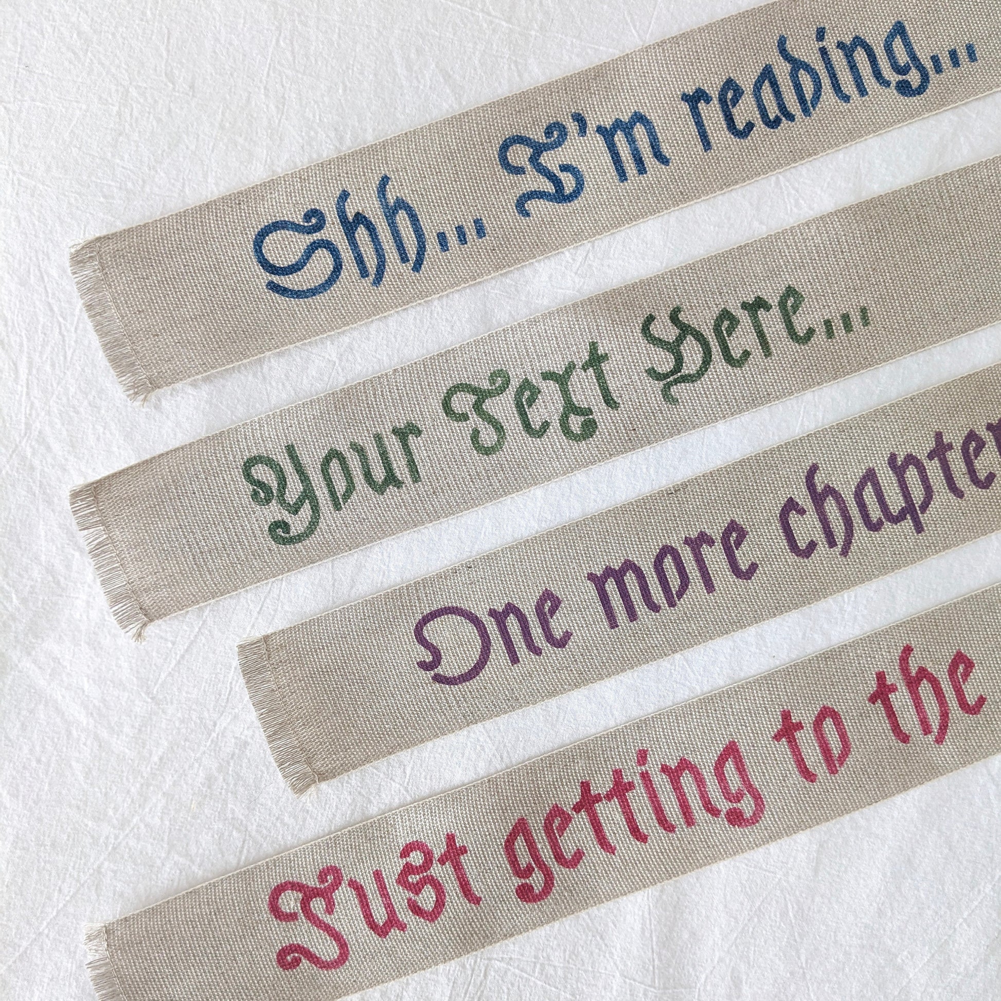 A hand painted linen ribbon bookmark that reads "Shh... I'm reading..." "Just getting to the good part..." or "One more chapter..."