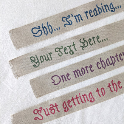 A hand painted linen ribbon bookmark that reads "Shh... I'm reading..." "Just getting to the good part..." or "One more chapter..."