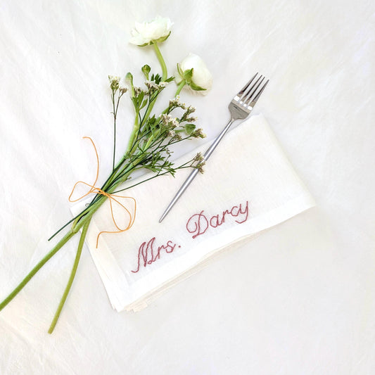 Hand embroidered linen napkin reading Mrs. Darcy in pink embroidery