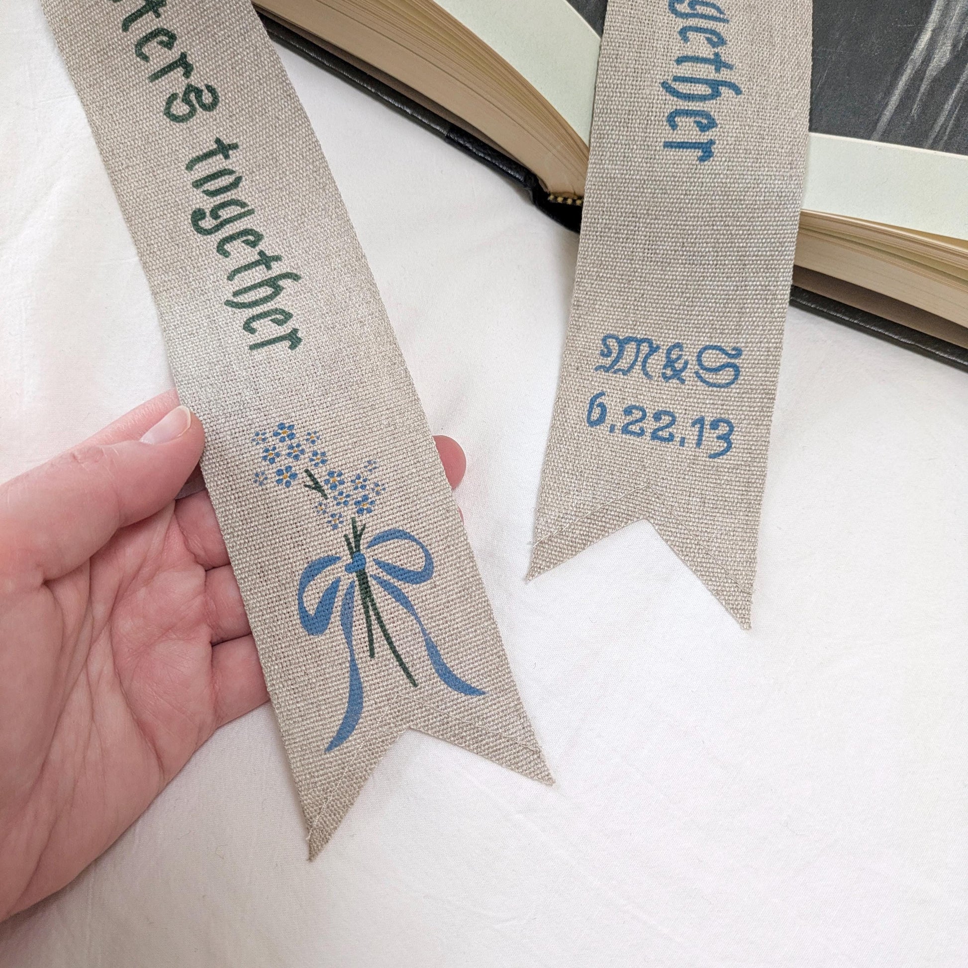 Hand painted linen ribbon bookmark that reads "To many more chapters together" with either initials and wedding anniversary date motif or forget-me-not-flower motif