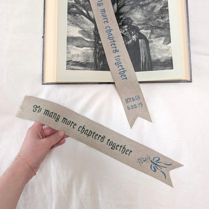 Hand painted linen ribbon bookmark that reads "To many more chapters together" with either initials and wedding anniversary date motif or forget-me-not-flower motif