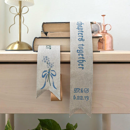 Hand painted linen ribbon bookmark that reads "To many more chapters together" with either initials and wedding anniversary date motif or forget-me-not-flower motif