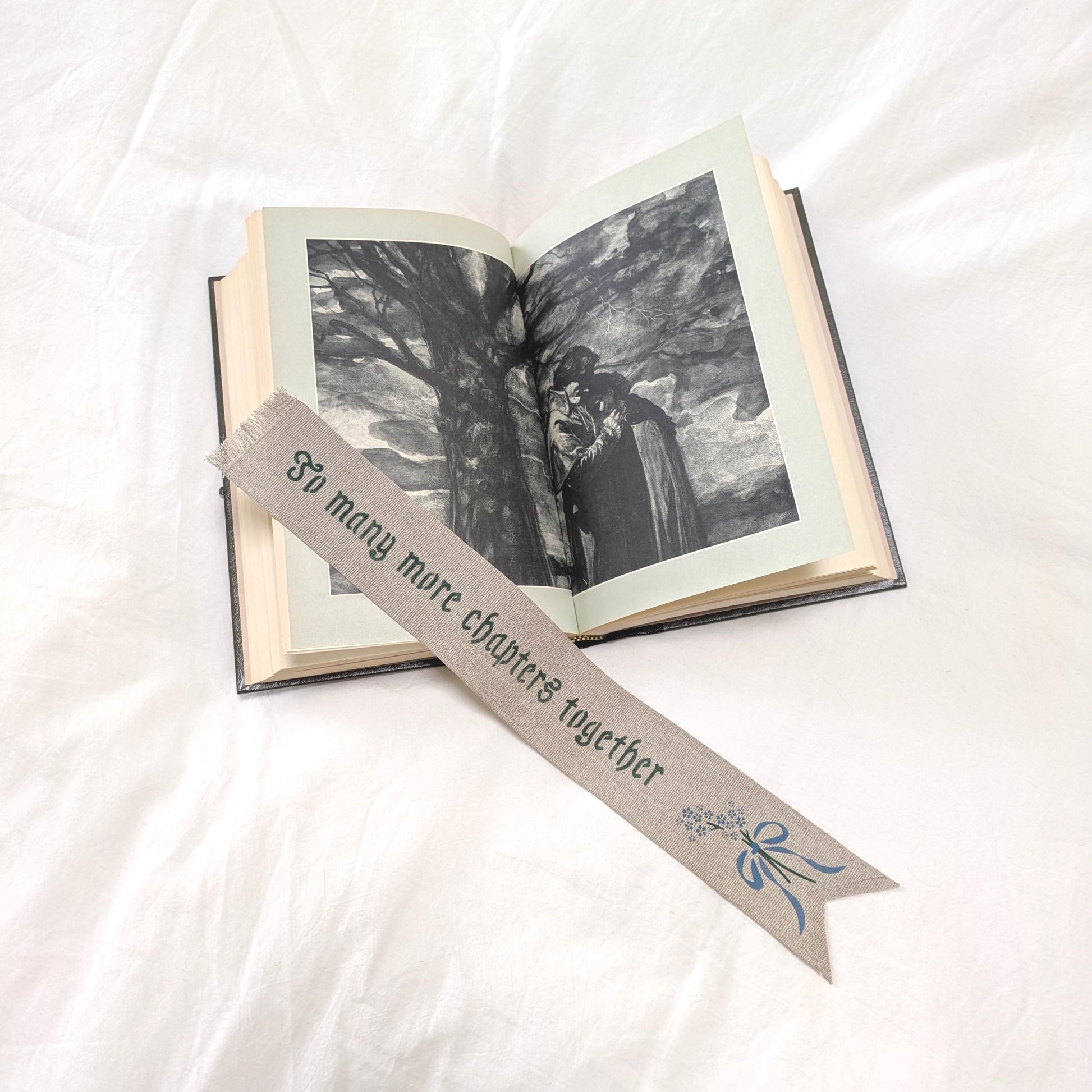 Hand painted linen ribbon bookmark that reads "To many more chapters together" with forget-me-not-flower motif